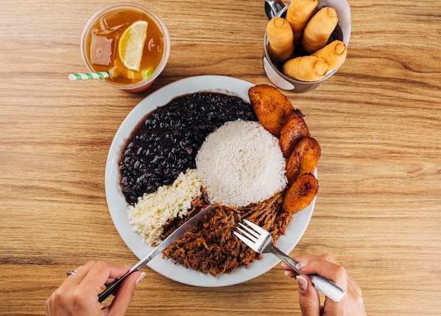 Foto ragazza che mangia un piatto di cibo venezuelano pabellon criollo ragazza che mangia un piatto di cibo venezuelano pabellon criollo riso bianco fagioli neri banane fritte manzo tritato e formaggio bianco latino