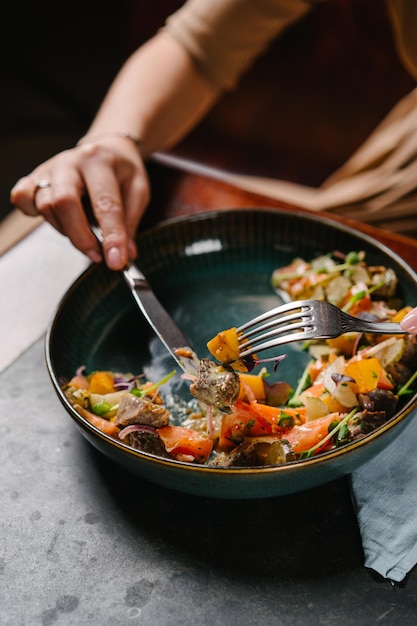 Girl eating salad with stewed veal cheeks potato wedges tomatoes and mustard sauce