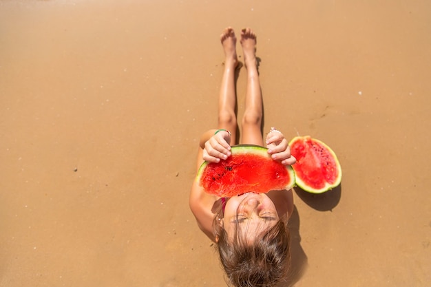 Girl eating a watermelon on the sand of the beach top view