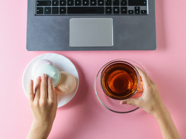 The girl eats a blue marshmallow with tea in front of the computer on a table