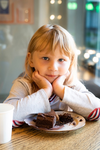 女の子はカフェでデザートにチョコレートケーキを食べる