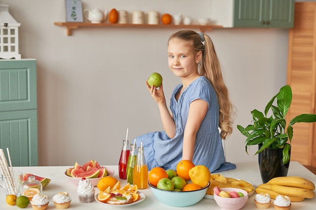 La ragazza mangia frutta su un tavolo pieno di cibo