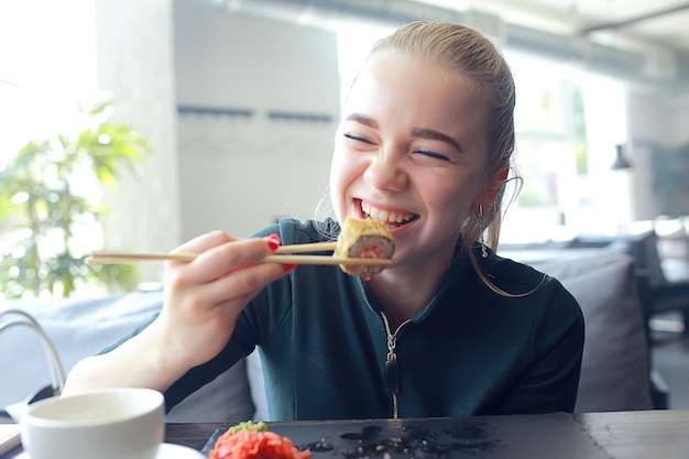 Ragazza mangia sushi e panini in un ristorante / cucina orientale, cibo giapponese, giovane modella in un ristorante