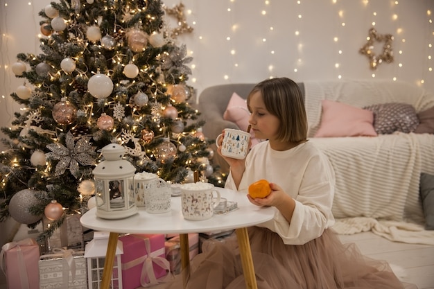 Girl eats tangerine next to Christmas tree