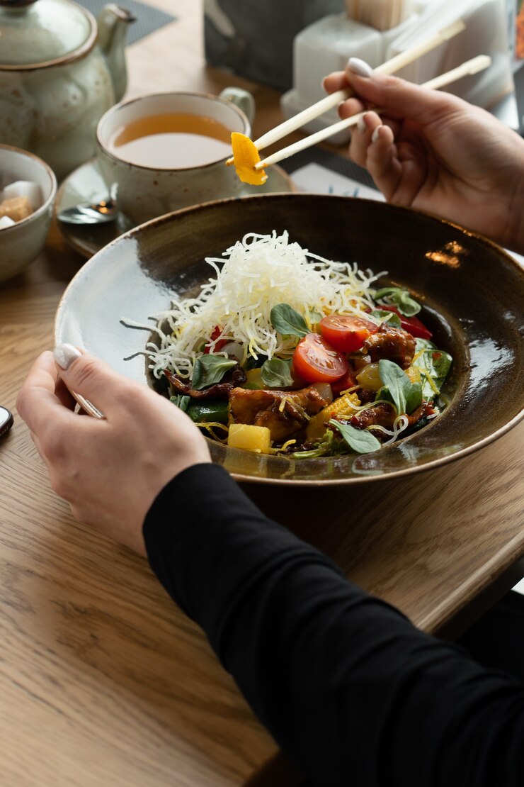 소녀는 젓가락으로 닭고기, 당근, 구운 옥수수, 치즈 및 체리 토마토와 함께 매운 아시아 야채 샐러드를 먹습니다. 필드의 얕은 깊이, 배경을 흐리게