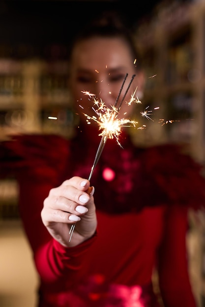 A girl in an elegant red dress holds sparklers in her hands