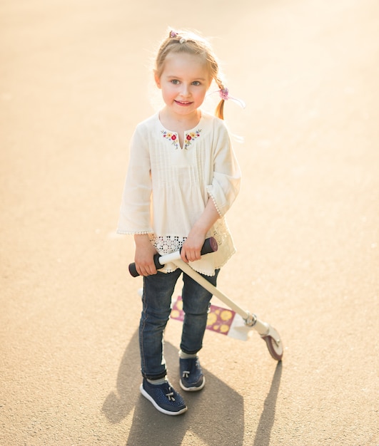 Girl in embroidered shirt playing with scooter