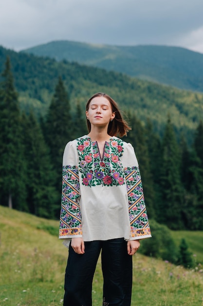 수놓은 셔츠를 입은 소녀는 우크라이나 산 풍경을 배경으로 반쯤 서 있다