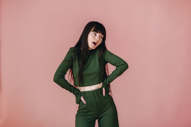 The girl emotionally poses and moves on a pink background in a green suit