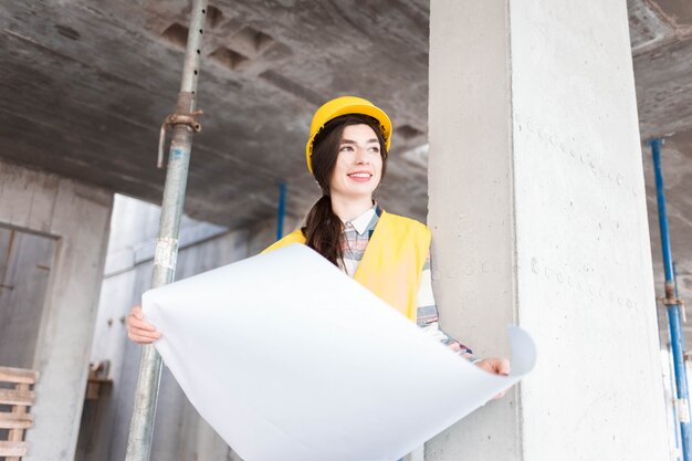 Девушка инженер на строительной площадке с чертежами в руках