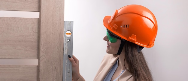 Una ragazza ingegnere con un casco da costruzione arancione con un livello di edificio installa le porte