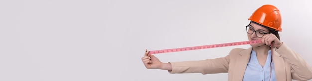 Girl engineer in an orange construction helmet with a measuring tape in her hands on a white background