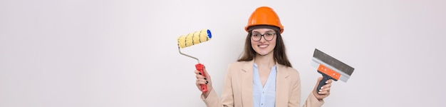 Girl engineer in an orange construction helmet with plastering painting tools in her hands on a white background