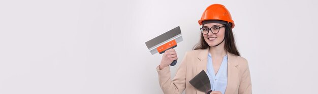 Girl engineer in an orange construction helmet with plastering painting tools in her hands on a white background