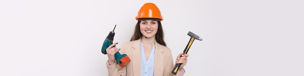 Девушка-инженер в оранжевом строительном шлеме с отверткой и молотком на белом фоне