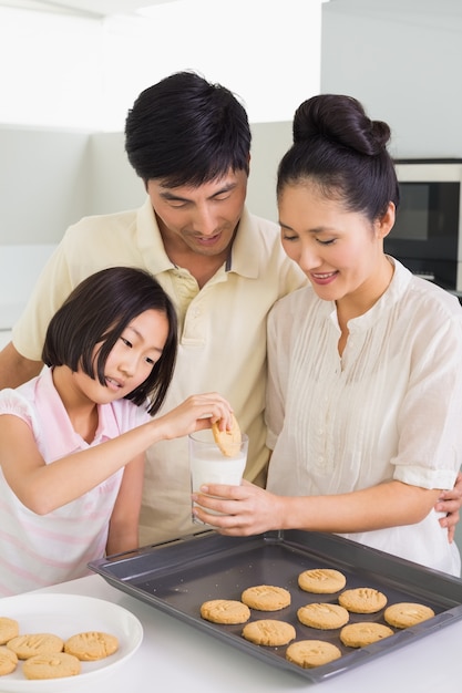 Girl enjoying cookies and milk with parents in kitchen