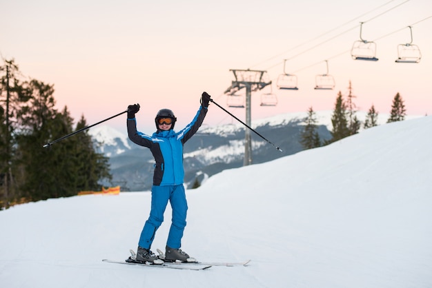 Girl enjoying ski holiday standing on the snowy mountain and raised her hands up. Woman at ski resort