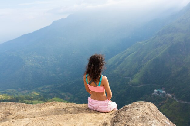 Girl enjoys a mountain view while standing on a cliff