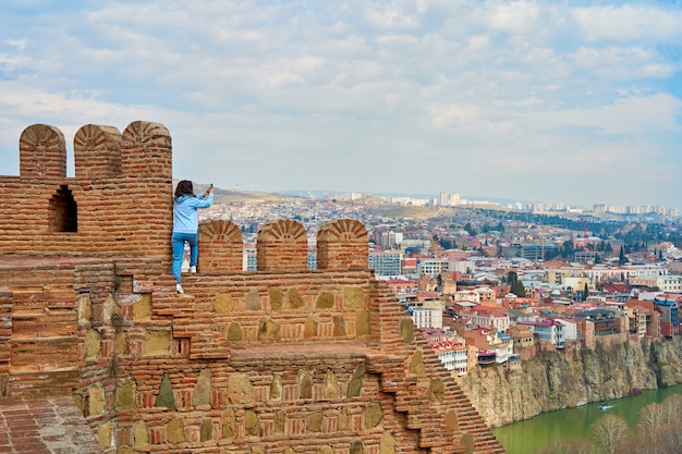 Foto la ragazza gode della vista e del silenzio mentre è seduta sul muro di un'antica fortezza che domina la città.