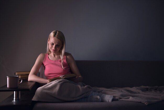 Girl enthusiastically reading a book best-selling house under a rug on a comfortable sofa with a lamp