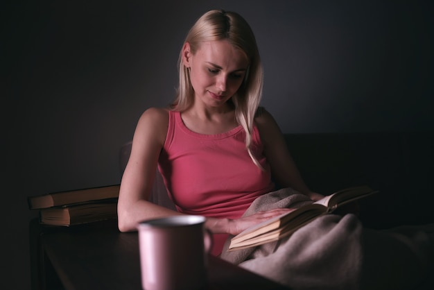 Girl enthusiastically reading a book best-selling house under a rug on a comfortable sofa with a lamp