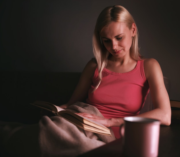 Girl enthusiastically reading a book best-selling house under a rug on a comfortable sofa with a lamp