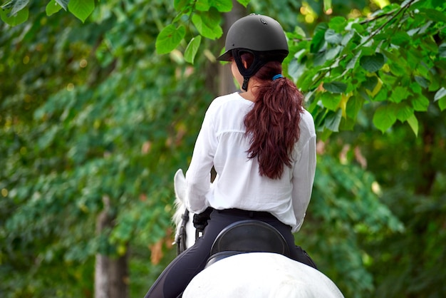 Girl in equestrian outfit riding a horse near trees