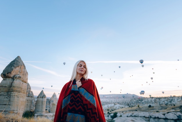 Girl in ethnic clothes at dawn watching the flight a lot of balloons fly over the valley of love