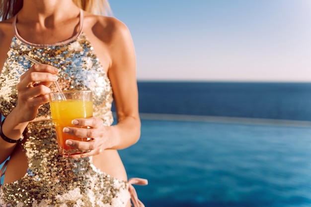 Girl in an expensive swimsuit with a cocktail in her hands spends her vacation near the pool at the resort