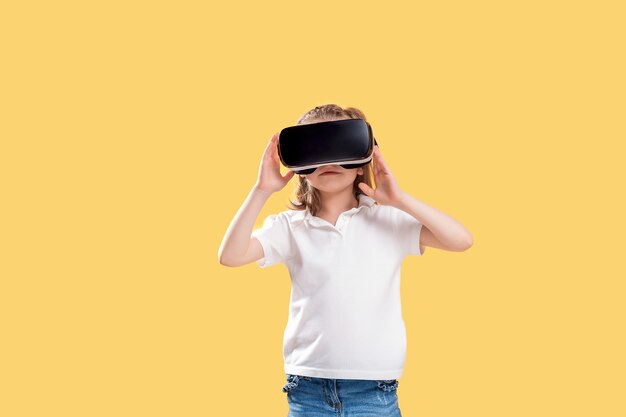 Девушка испытывая игру шлемофона VR на желтом цвете. Удивлены эмоции на ее лице. Ребенок использует игровой гаджет для виртуальной реальности.