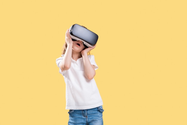 Girl   experiencing VR headset game on yellow . Surprised emotions on her face.Child using a gaming gadget for virtual reality.