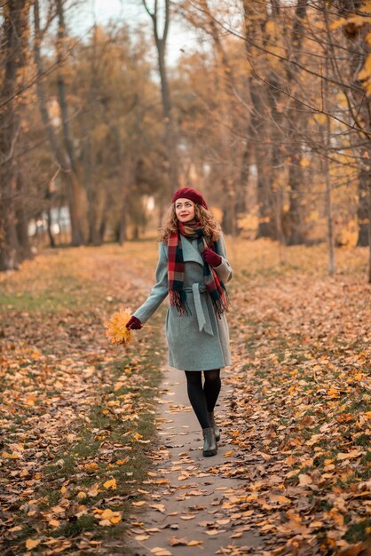 Girl on fabulous background of park with orange autumn leaves in hands walking on road