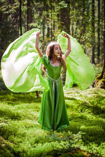 おとぎ話のエルフのドレスを着た少女は、羽ばたきながら森の中を裸足で歩きます