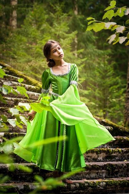 La ragazza in un vestito da elfo da favola cammina a piedi nudi attraverso la foresta scendendo le rune di un'antica scala