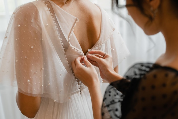 The girl fastens the buttons on the bride's beautiful wedding dress