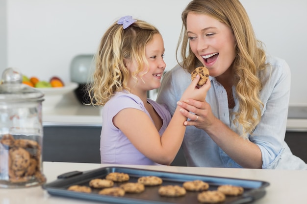 Girl feeding cookie to mother at counter