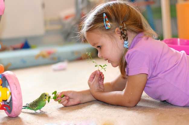 The girl feeds parrot fresh grass Green budgerigar