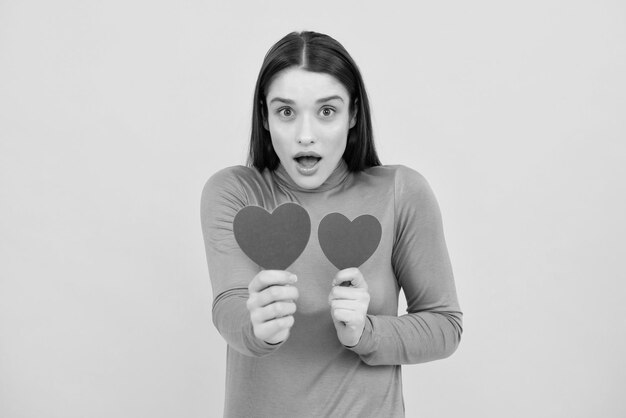 Girl feeling love Portrait of attractive lovely cheerful girl holding in hands paper heart isolated over yellow background Love valentine concept