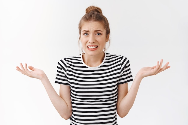 Girl feeling sorry and guilty for causing trouble, squinting and shrugging with hands spread sideways, standing troubled and clueless, cant understand how accident happened, white background