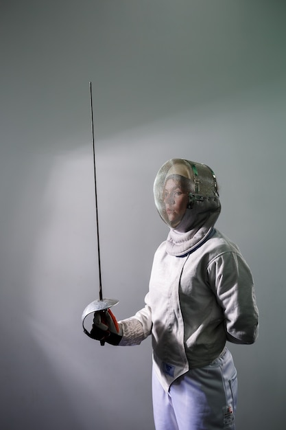 Girl in a fencing costume with a sword in hand isolated on white studio background. Young girls practice and exercise. Sports, healthy lifestyle.