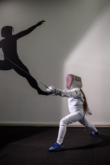 A girl in a fencing suit with a sword in hand. Young female model practicing and exercising. Sports, healthy lifestyle.