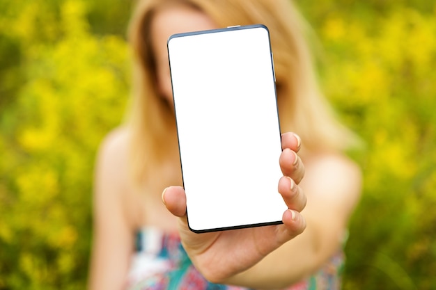 Girl in the field, shows a black phone, close-up. Girl in the field with phone.