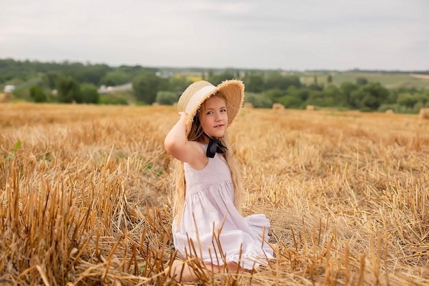 A girl in a field wearing a hat sits in a field.