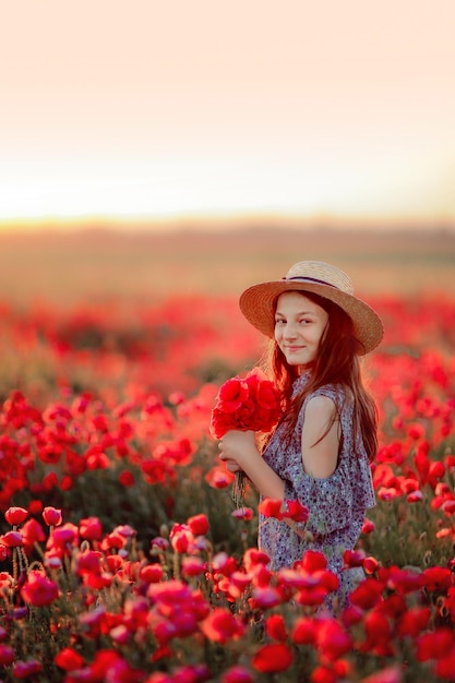 a girl in a field with poppies in a hat smiles