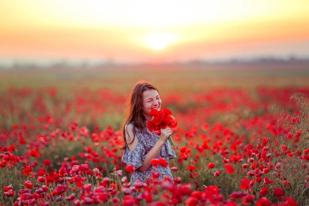 A girl in a field with poppies in her hands smiles