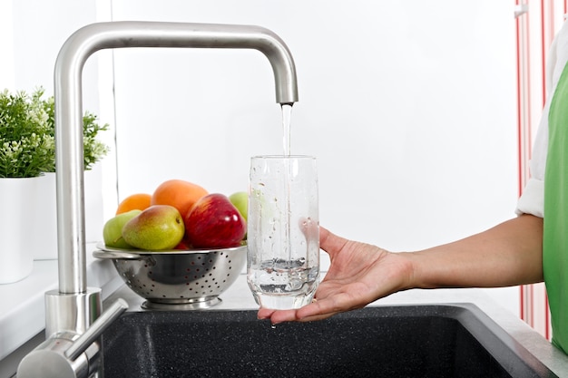 The girl fills a glass with water from a water tap in the kitchen