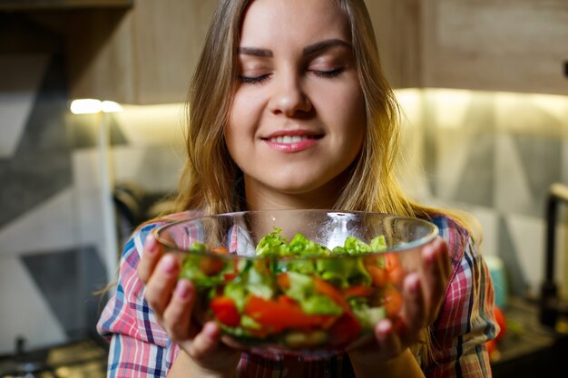 女の子のフィットネストレーナーの菜食主義の栄養士は、キッチンで新鮮な野菜のサラダを準備します。彼女の姿を見ている