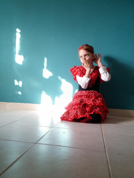 Foto ragazza in costume di danza flamenco accovacciata sul pavimento a casa