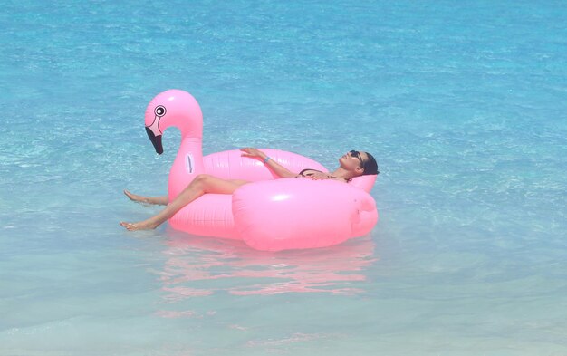 girl floats on an inflatable pink flamingo in the ocean