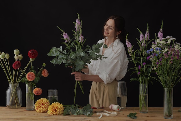 女の子の花屋はフローリストの暗い背景のレイアウトで花のワーク ショップで花束を収集します